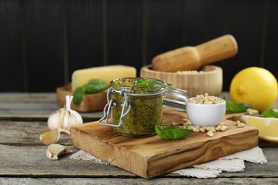 Photo of Delicious pesto sauce in jar and ingredients on wooden table. Space for text