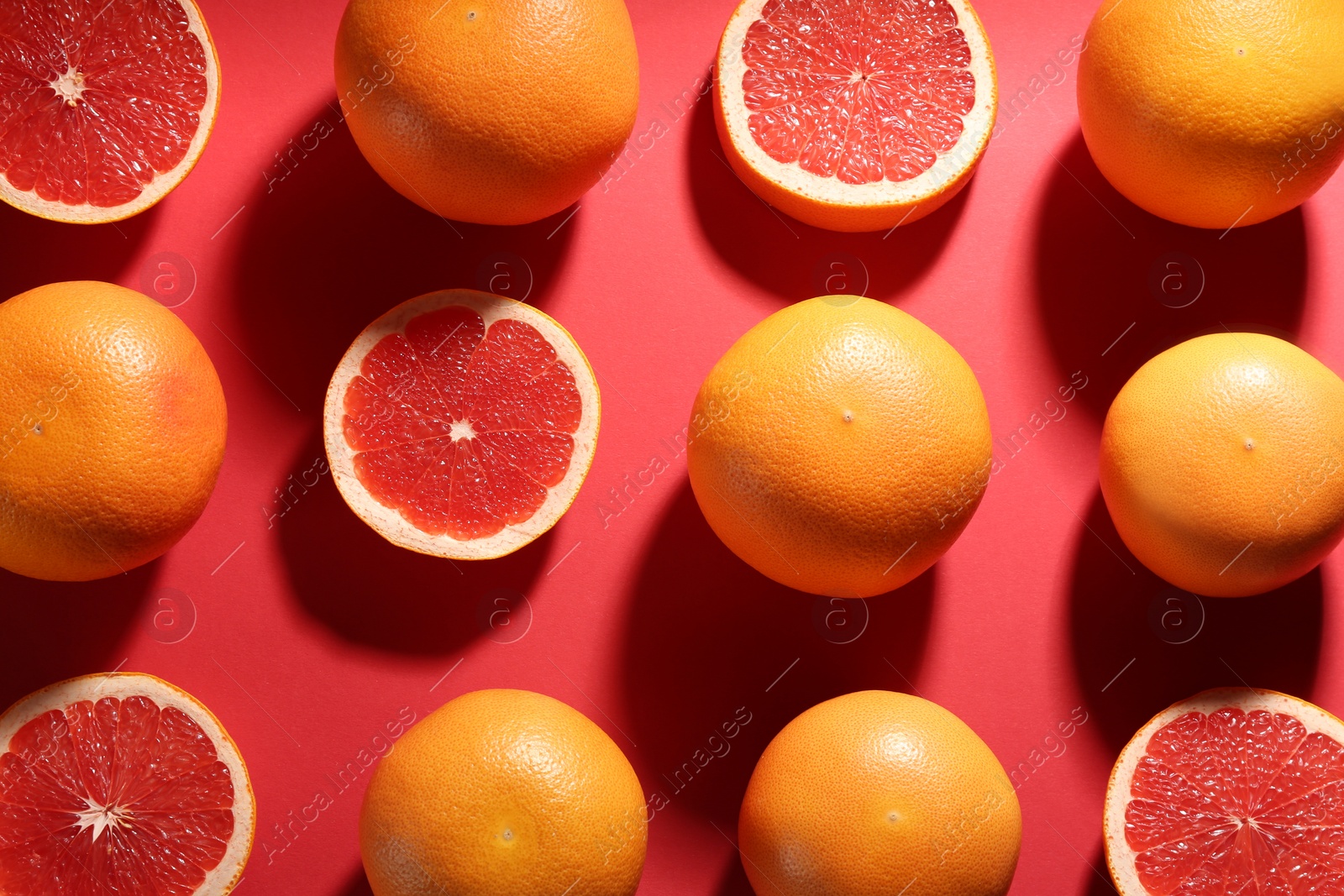 Photo of Cut and whole ripe grapefruits on red background, flat lay