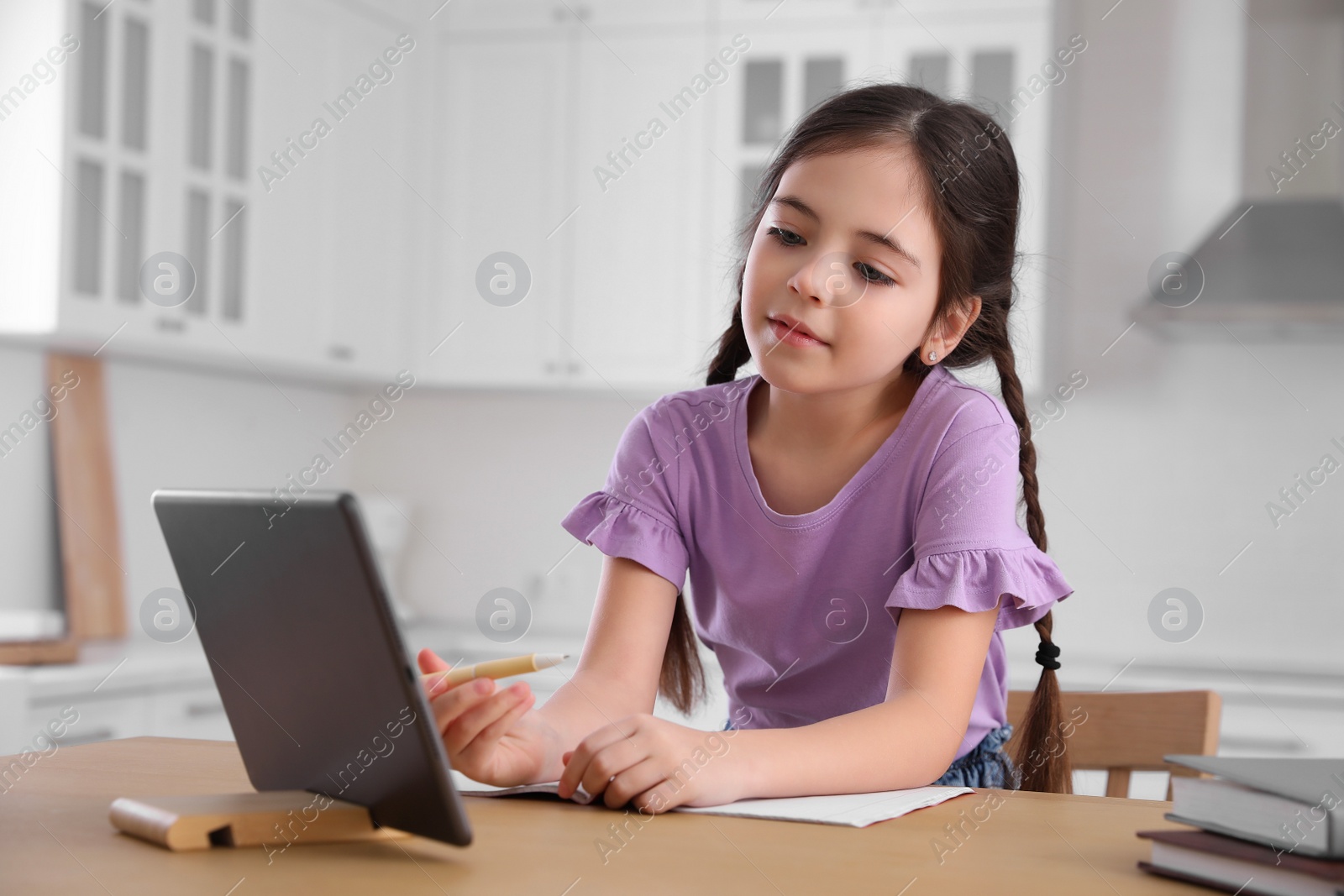 Photo of Little girl doing homework with modern tablet at home