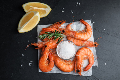 Photo of Delicious cooked shrimps with rosemary, lemon and salt on black table, flat lay