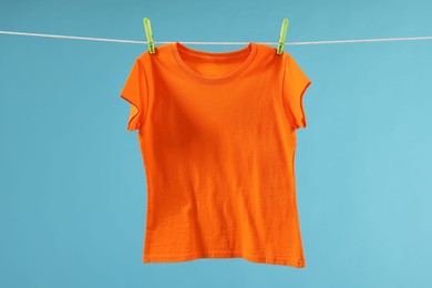 Photo of One orange t-shirt drying on washing line against light blue background