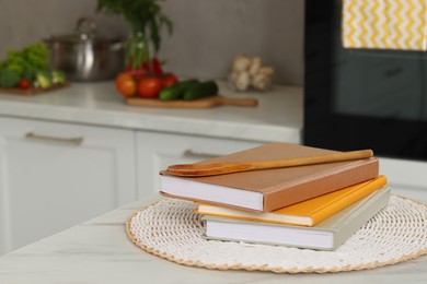 Photo of Recipe books and wooden spoon on white marble table in kitchen, closeup. Space for text