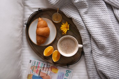 Photo of Wooden tray with delicious breakfast and beautiful flower on bed, flat lay