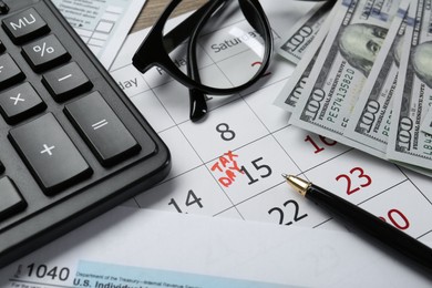 Photo of Calendar with date reminder about tax day, documents, money, pen, calculator and glasses on table, closeup