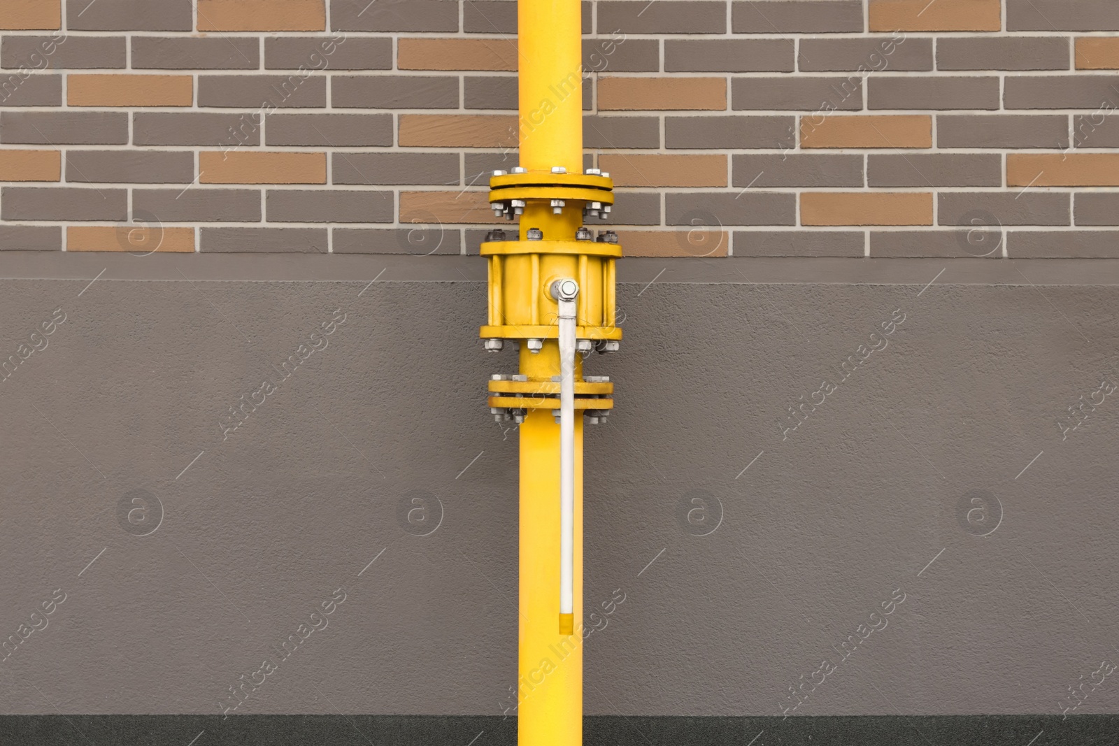 Photo of Yellow gas pipe with valve near brick wall outdoors