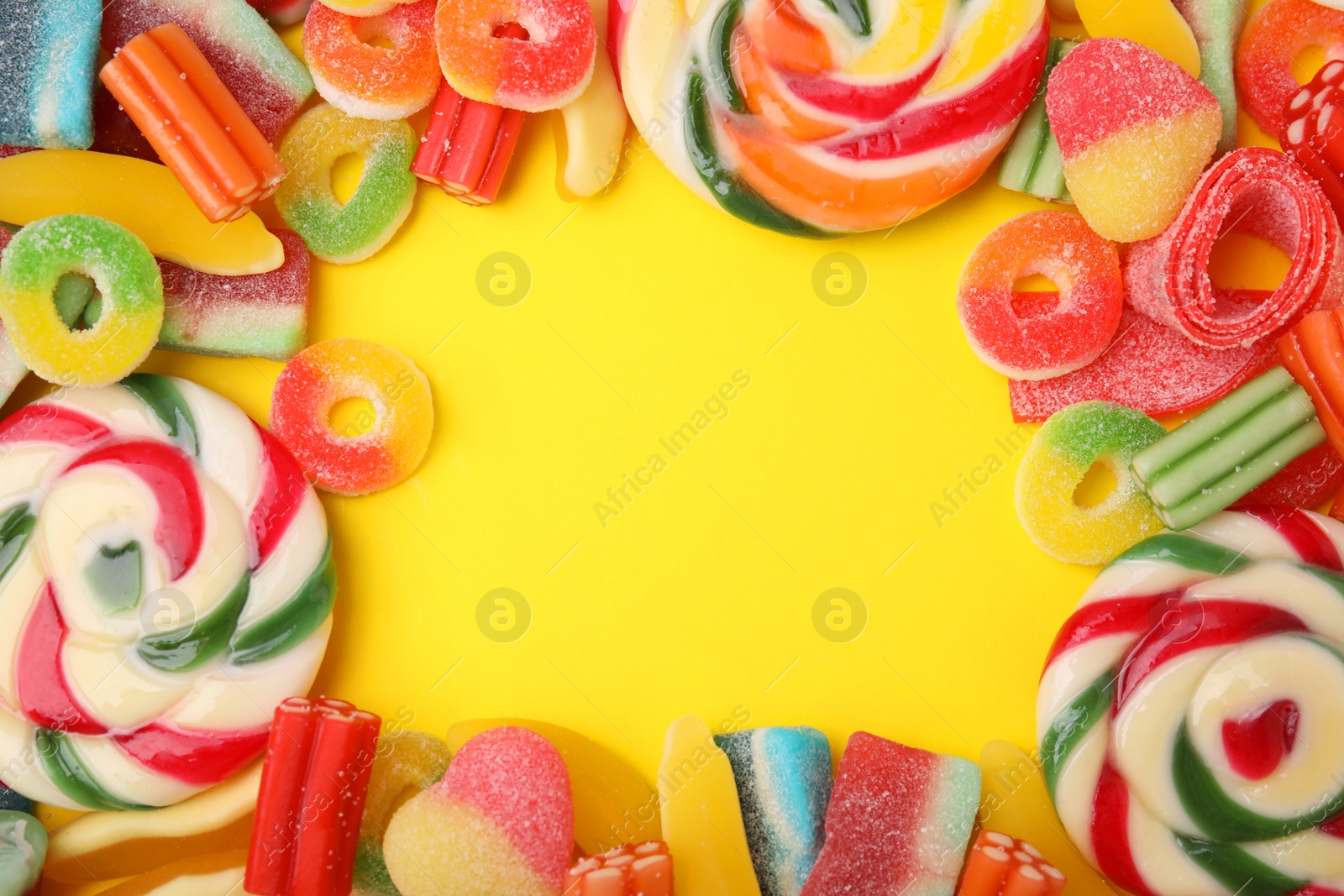Photo of Frame of many different jelly candies on yellow background, flat lay. Space for text