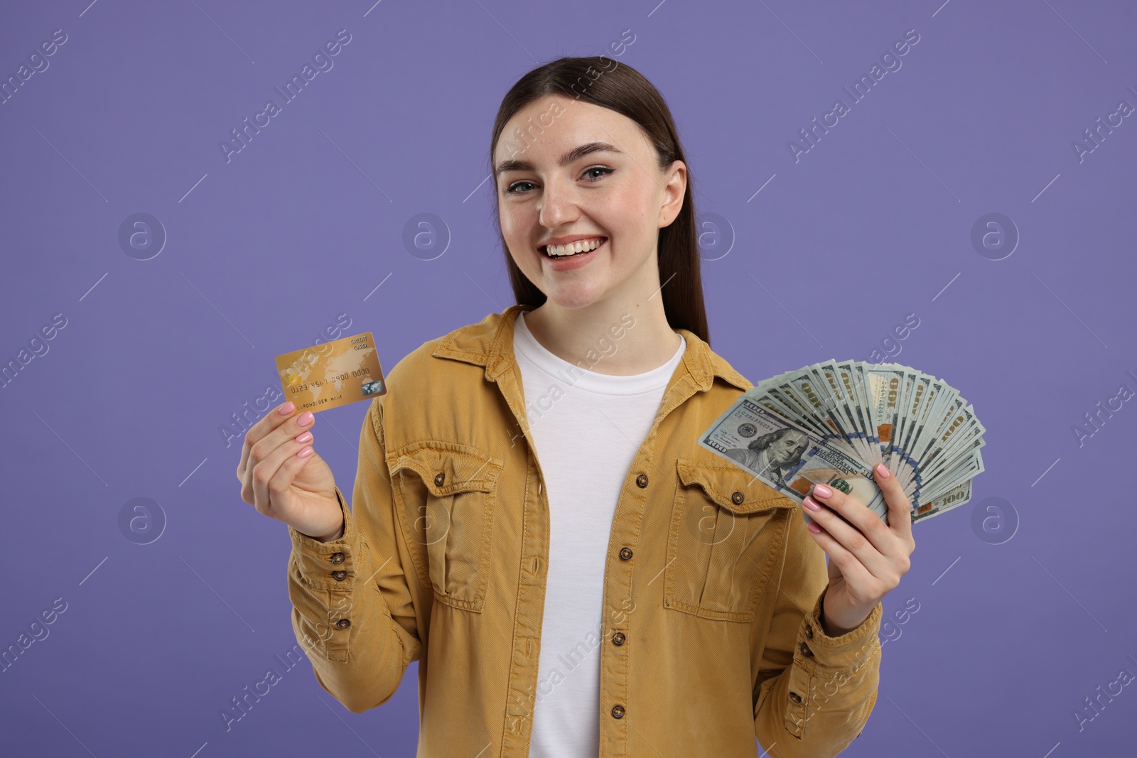 Photo of Happy woman with credit card and dollar banknotes on purple background