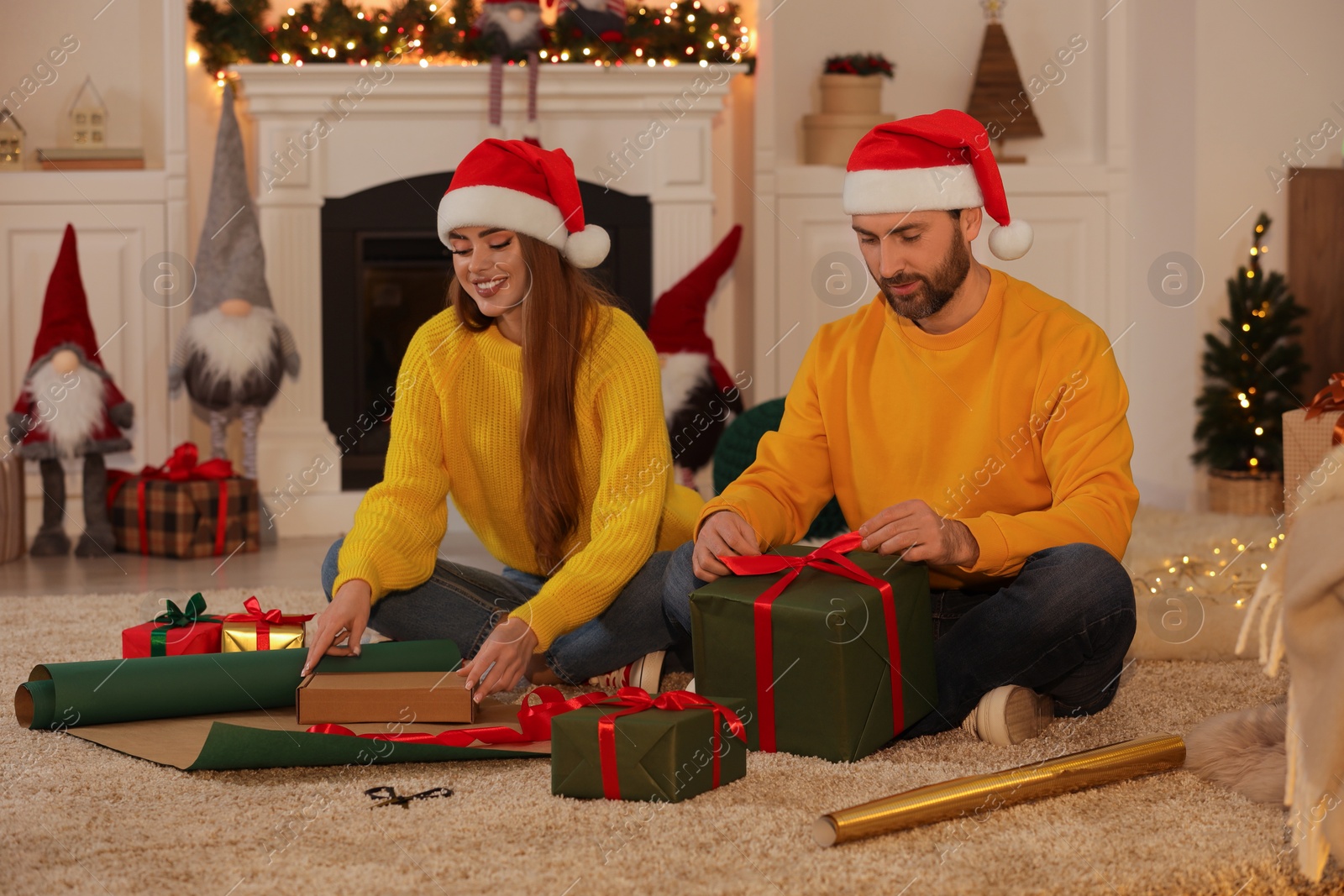 Photo of Happy couple in Santa hats decorating Christmas gifts at home