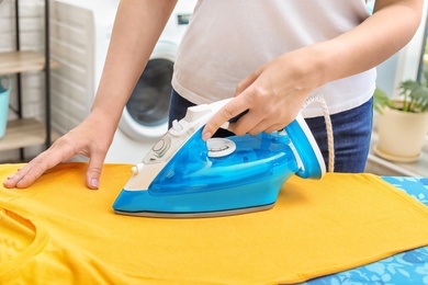 Woman ironing clothes on board indoors, closeup