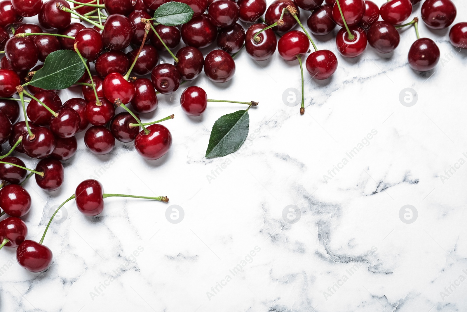 Photo of Sweet juicy cherries on white marble table, flat lay. Space for text
