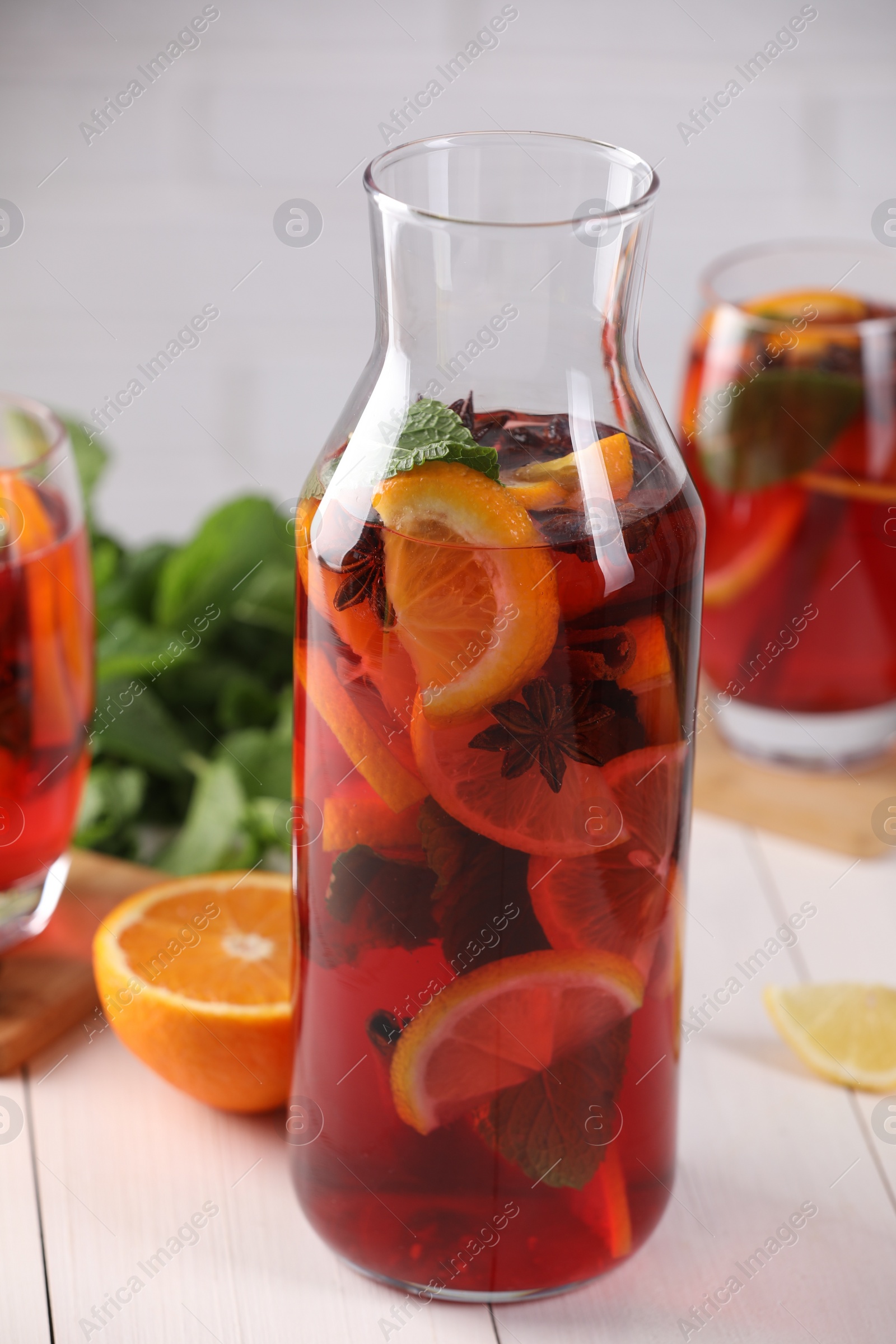 Photo of Delicious punch drink and slices of fruits on white wooden table, closeup