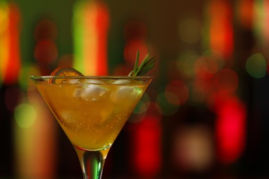 Photo of Martini glass with cocktail, ice cubes and rosemary in bar, closeup. Space for text