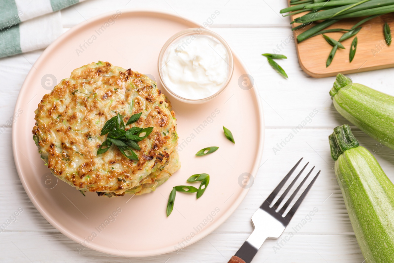 Photo of Delicious zucchini fritters served on white wooden table, flat lay