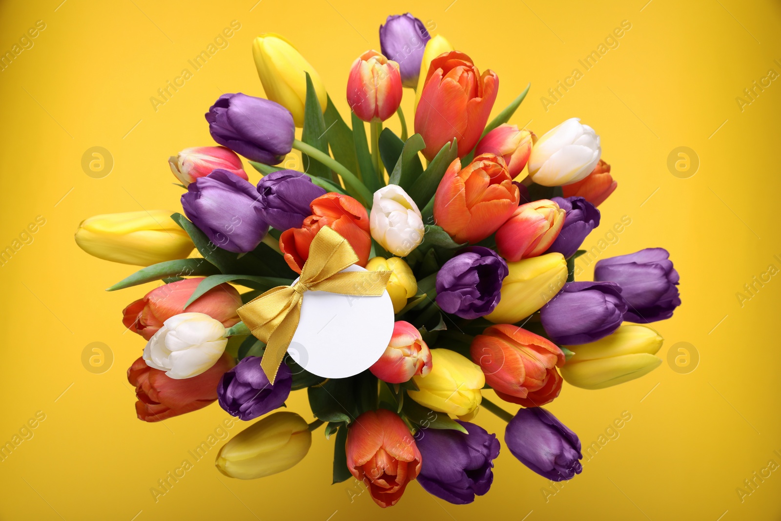 Photo of Bouquet of beautiful colorful tulips with blank card on yellow background, top view. Birthday celebration