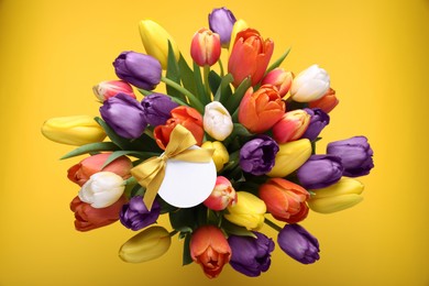 Bouquet of beautiful colorful tulips with blank card on yellow background, top view. Birthday celebration