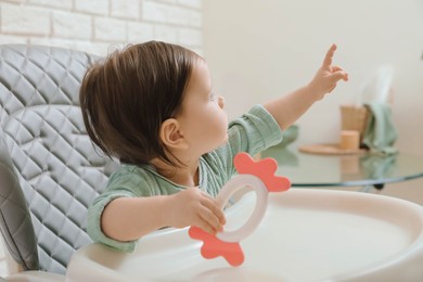 Cute little baby with teether in high chair indoors