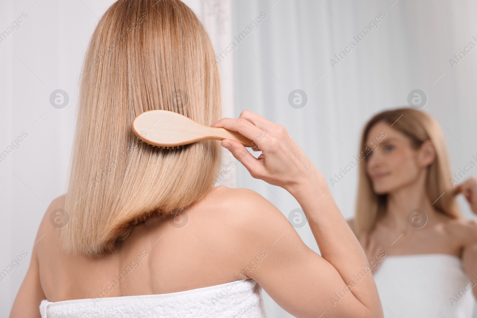 Photo of Woman brushing her hair near mirror in room, back view