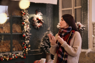 Photo of Beautiful woman using mobile phone in decorated cafe. Christmas celebration