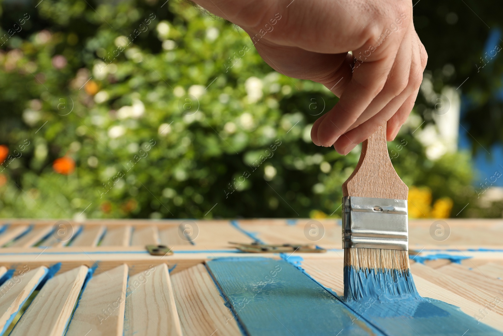 Photo of Man painting wooden surface with blue dye outdoors, closeup. Space for text