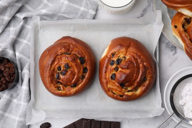 Delicious rolls with raisins on white marble table, flat lay. Sweet buns