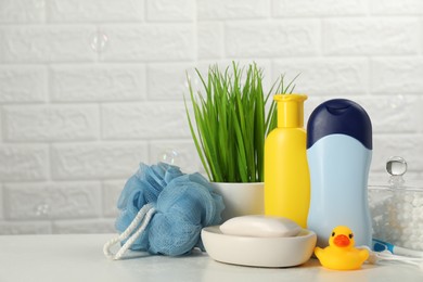 Different baby bath accessories and cosmetic products on white table against brick wall, space for text