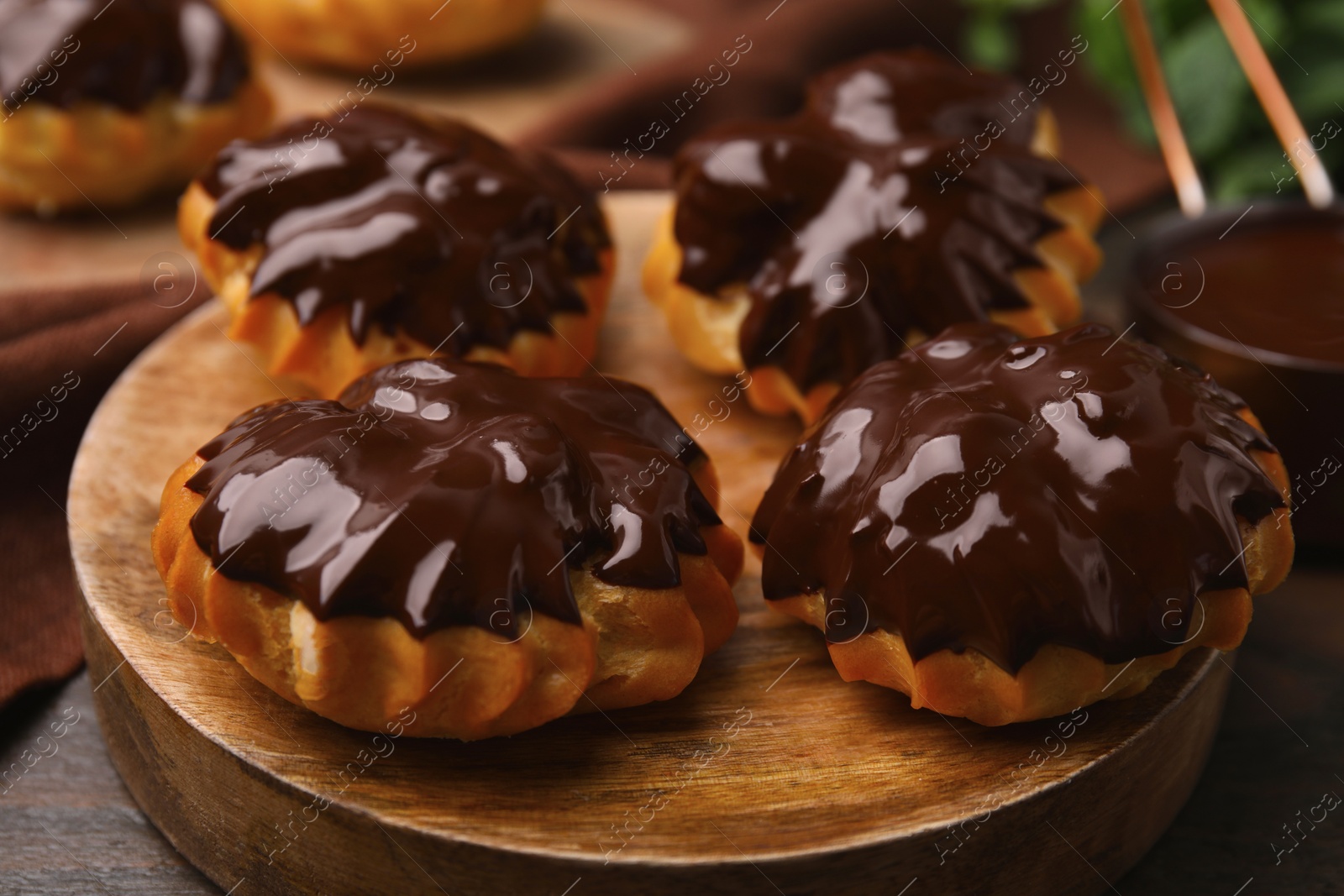 Photo of Delicious profiteroles with chocolate spread on wooden board, closeup