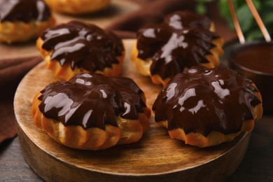 Photo of Delicious profiteroles with chocolate spread on wooden board, closeup