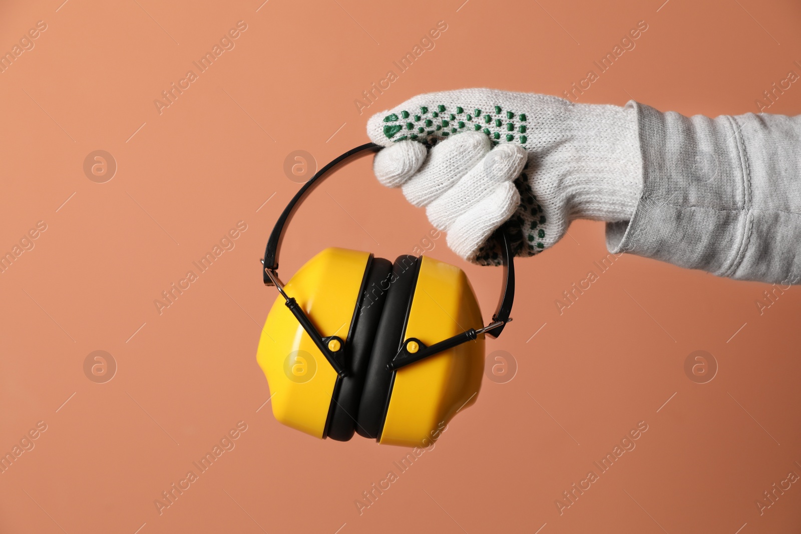 Photo of Worker holding safety headphones on coral background, closeup. Hearing protection device