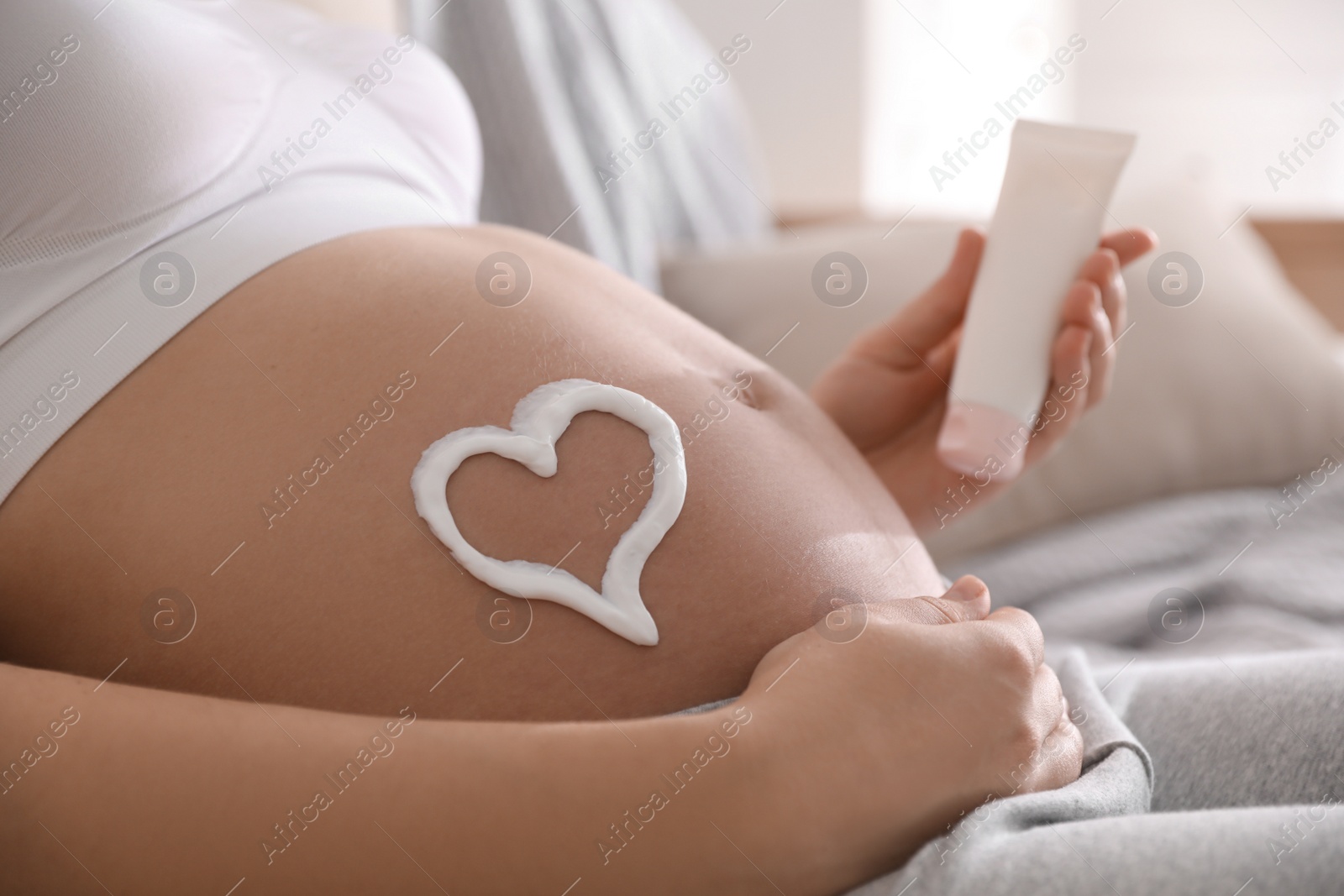 Photo of Young pregnant woman with cosmetic product indoors, closeup