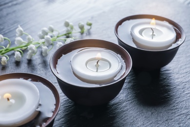 Photo of Burning candles in bowls with water on table
