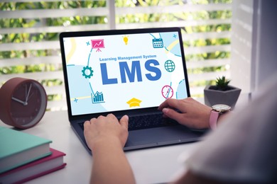 Image of Learning management system. Woman working with modern laptop at table, closeup. Different icons and abbreviation LMS on screen