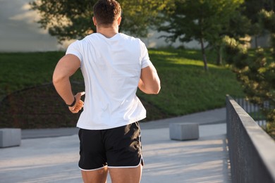 Photo of Man running outdoors on sunny day, back view