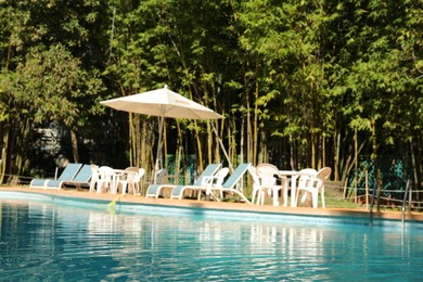 Photo of Pool with clean water, sunbeds and parasol outdoors