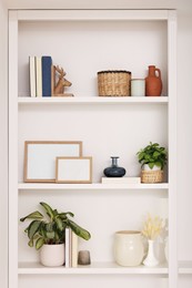 Photo of Interior design. Shelves with stylish accessories, potted plants and frames near white wall