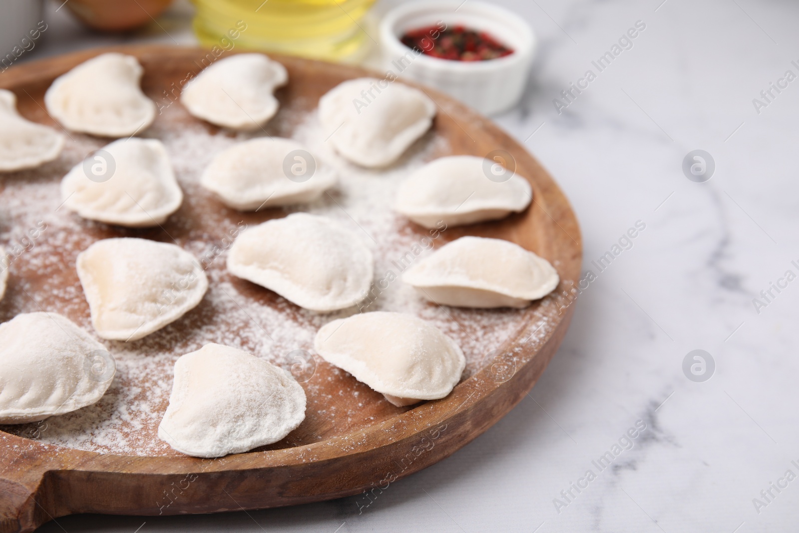 Photo of Raw dumplings (varenyky) with tasty filling and flour on white marble table, closeup