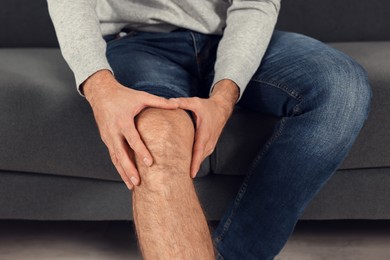 Photo of Man suffering from leg pain on sofa indoors, closeup