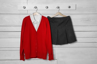 Photo of Shirt, jumper and skirt hanging on white wooden wall. School uniform