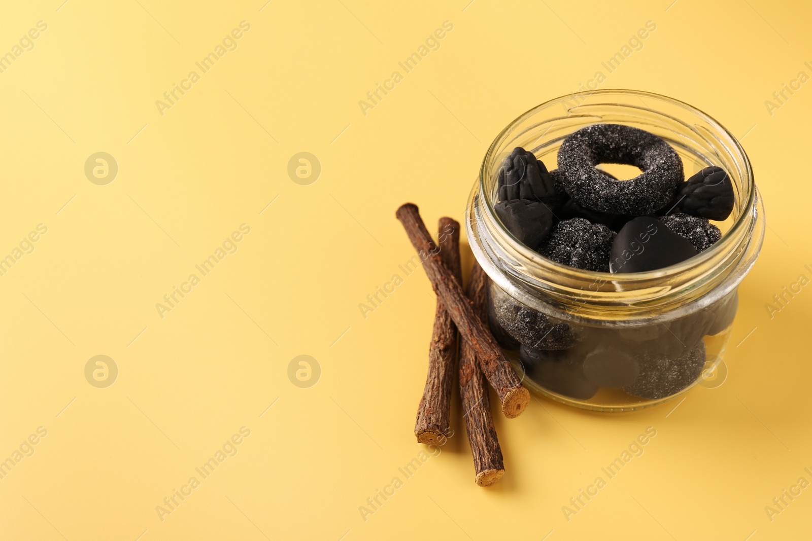 Photo of Jar with tasty candies and dried liquorice roots on yellow background. Space for text