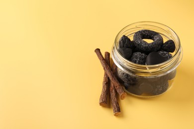 Jar with tasty candies and dried liquorice roots on yellow background. Space for text