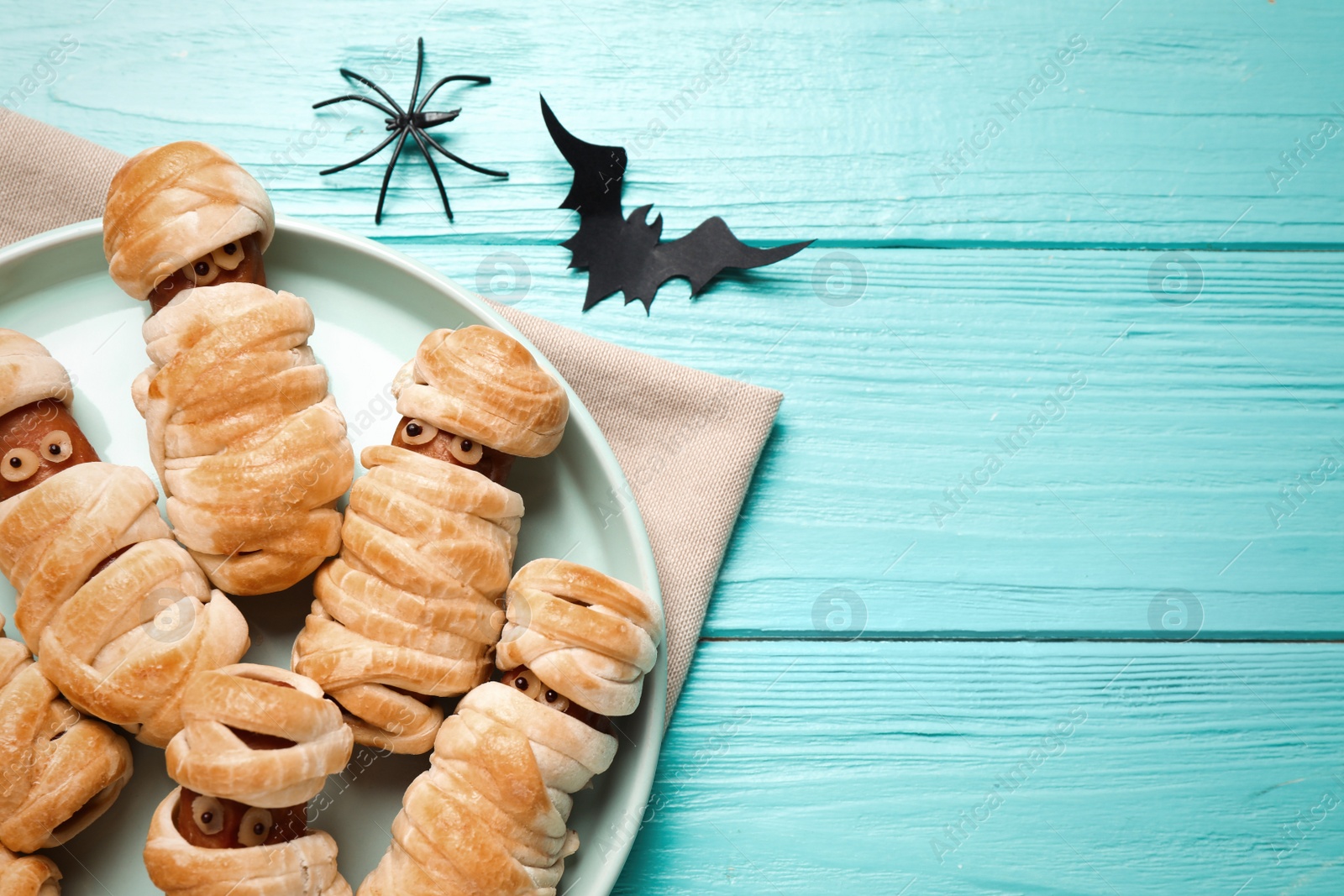 Photo of Spooky sausage mummies for Halloween party served on light blue wooden table, flat lay. Space for text