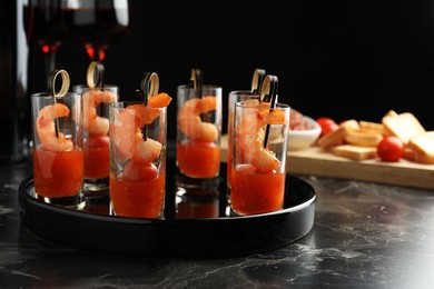 Photo of Tasty canapes with shrimps, tomatoes and sauce in shot glasses on black marble table, closeup