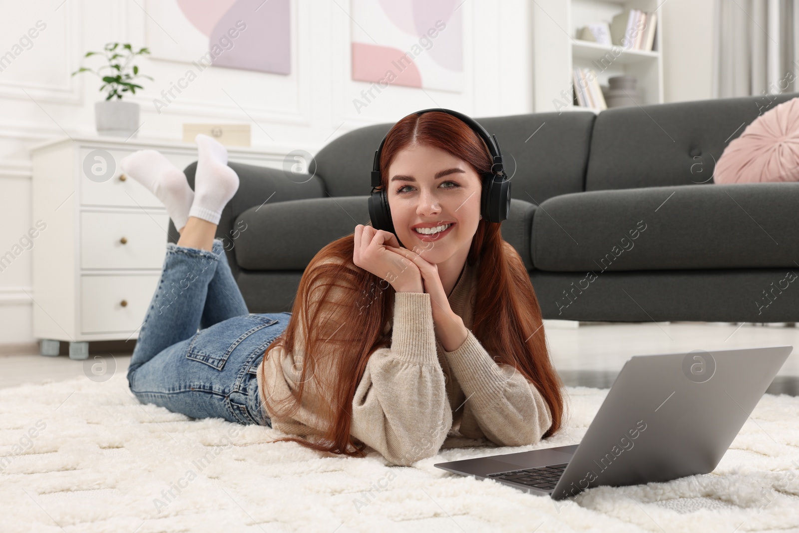 Photo of Happy woman with headphones and laptop on rug in living room