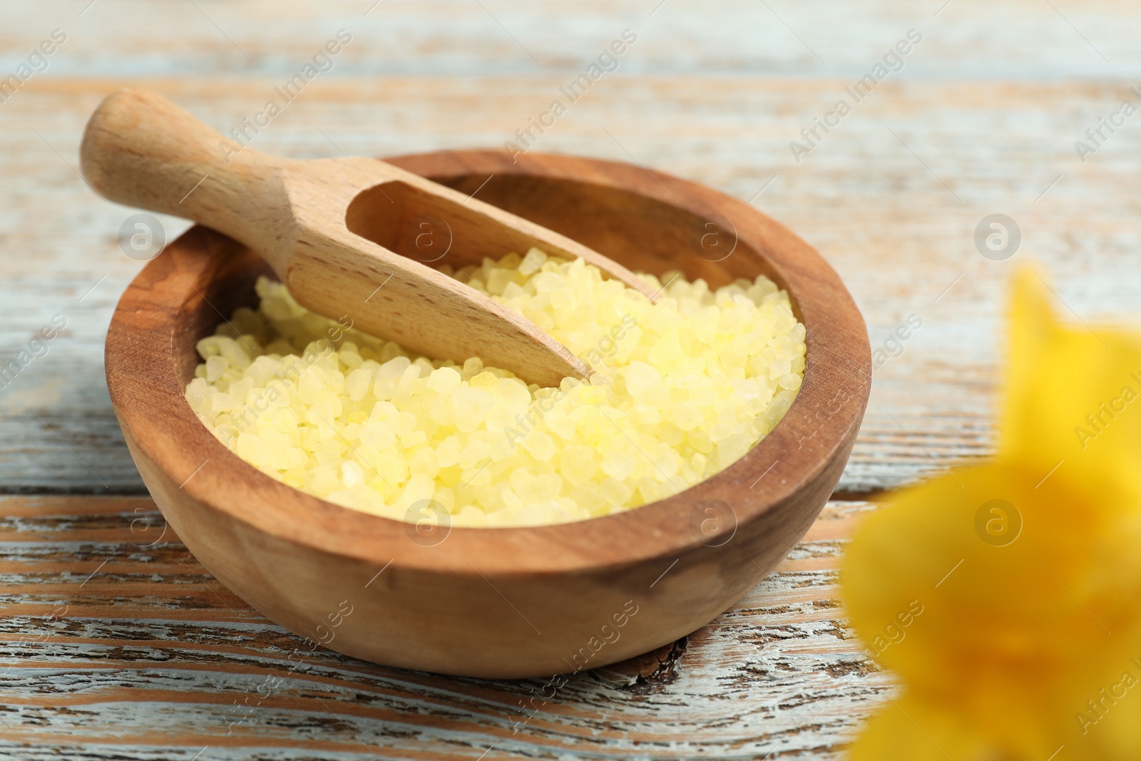 Photo of Yellow sea salt in bowl and scoop on wooden table, closeup