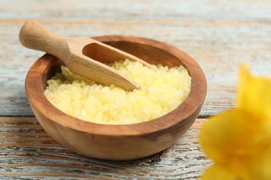 Yellow sea salt in bowl and scoop on wooden table, closeup