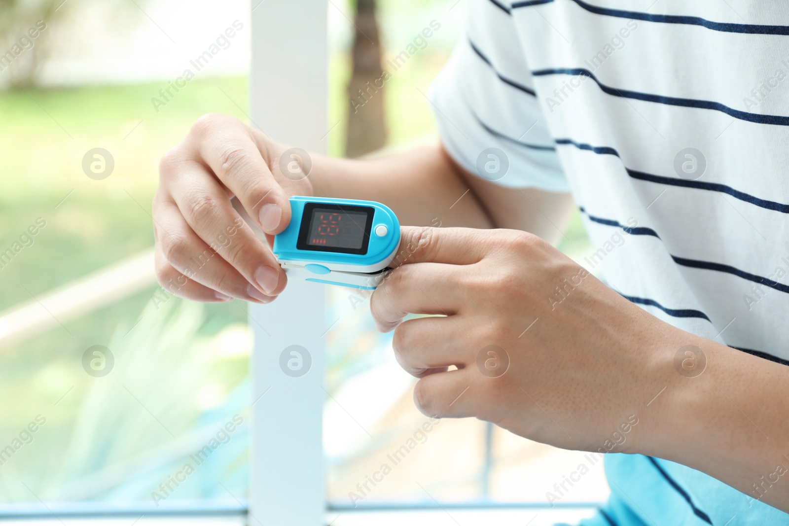Photo of Young man checking pulse with blood pressure monitor on finger against blurred background, closeup
