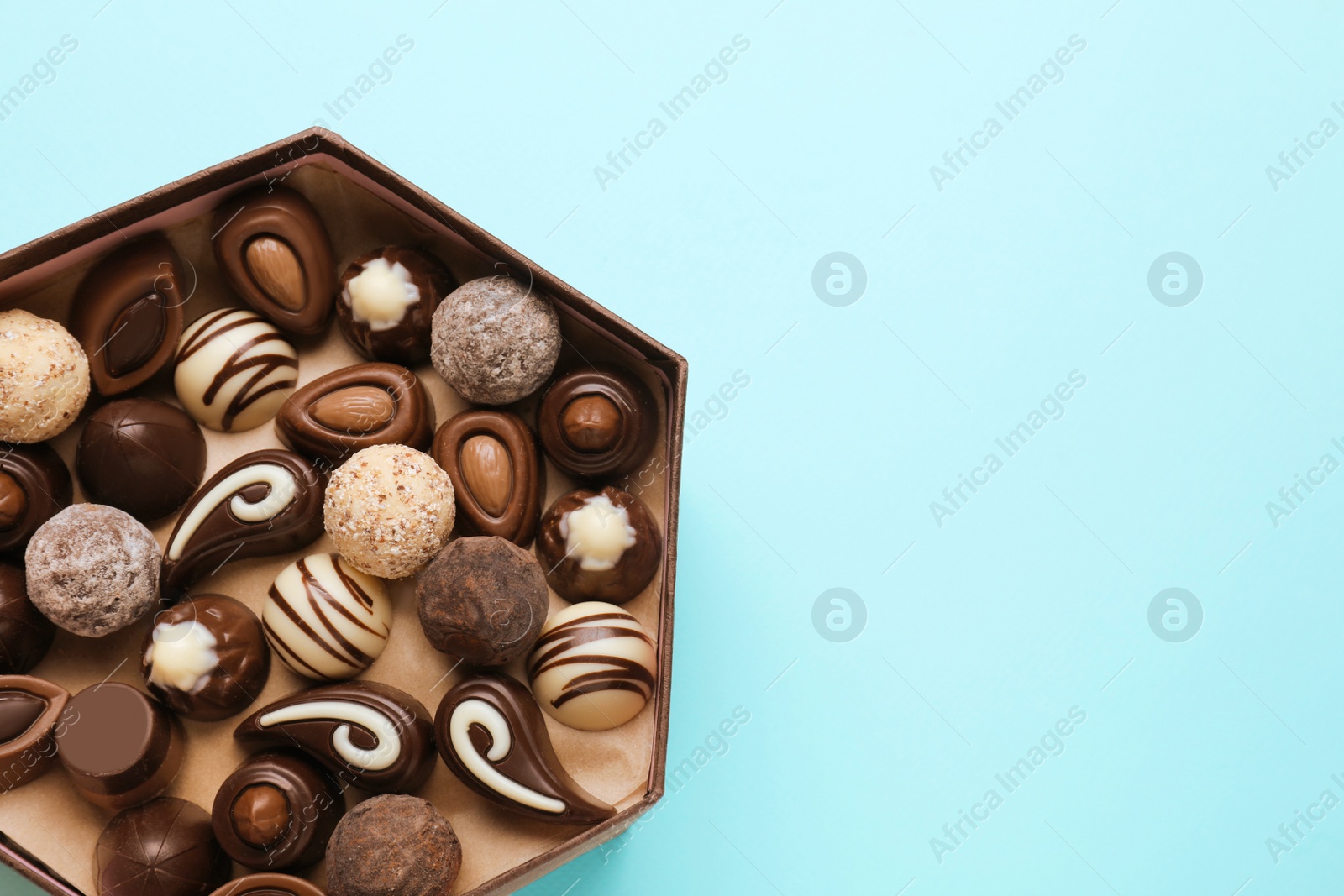 Photo of Box of delicious chocolate candies on light blue background, top view. Space for text