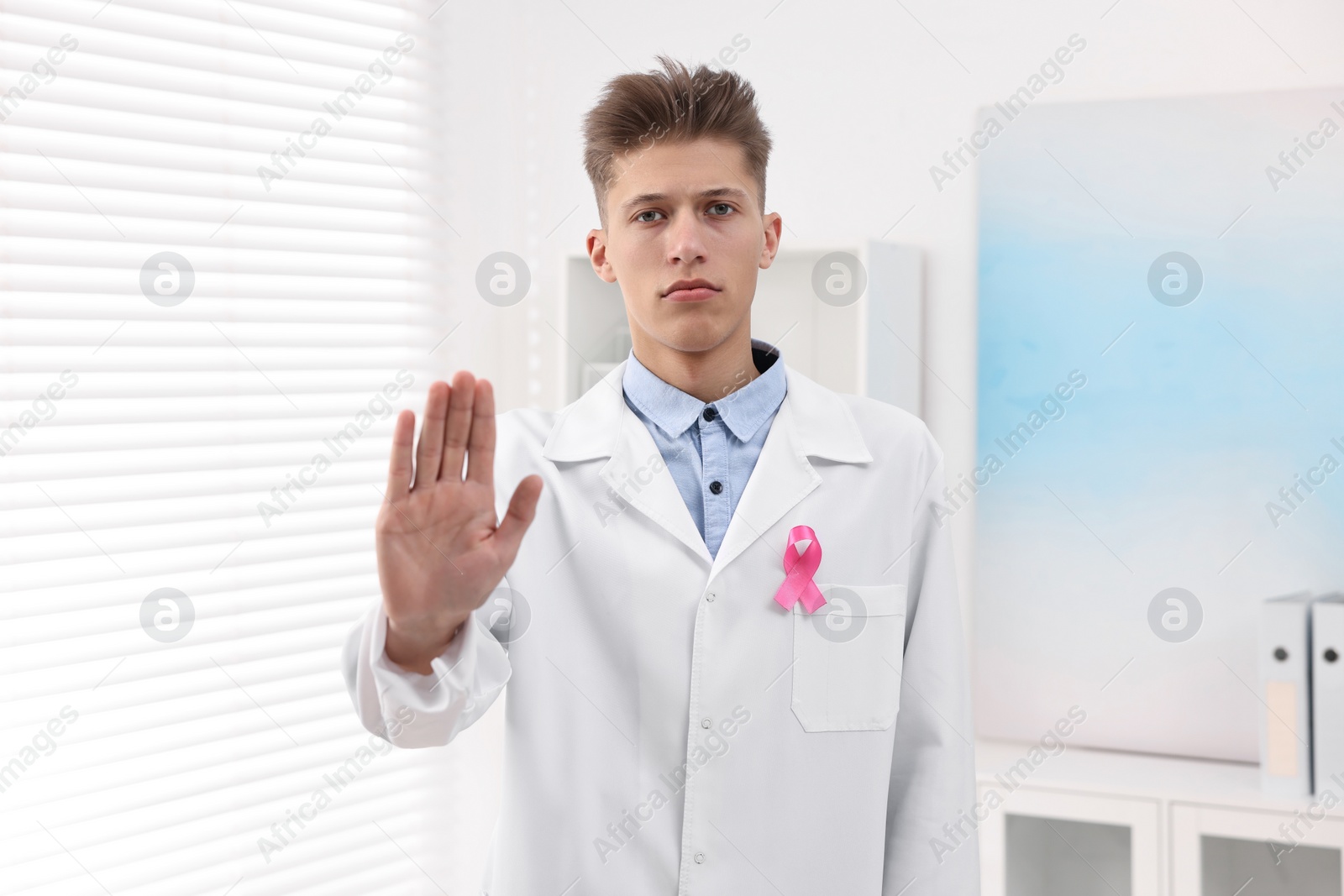 Photo of Mammologist with pink ribbon showing stop gesture in hospital. Breast cancer awareness