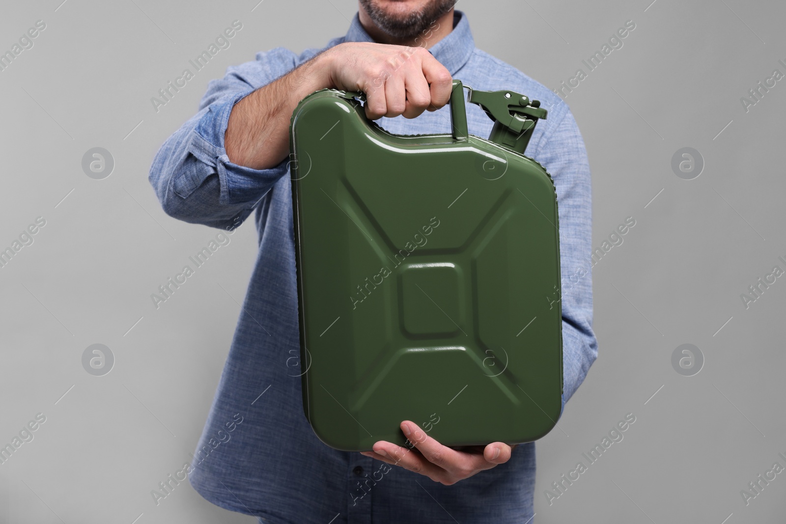 Photo of Man holding khaki metal canister on light grey background, closeup