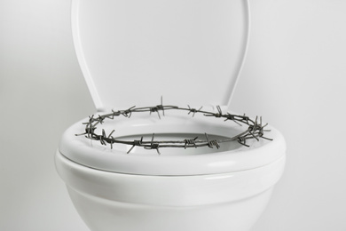 Toilet bowl with barbed wire on white background. Hemorrhoids concept