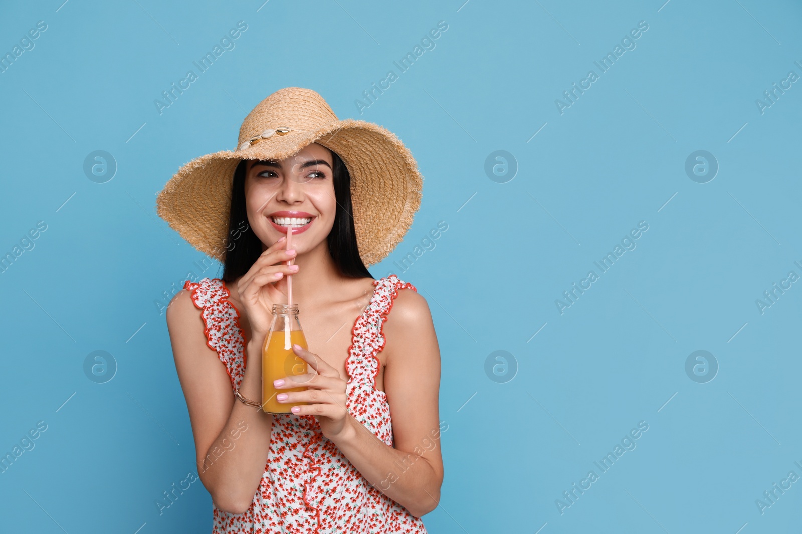 Photo of Beautiful young woman with straw hat and bottle of refreshing drink on light blue background. Space for text